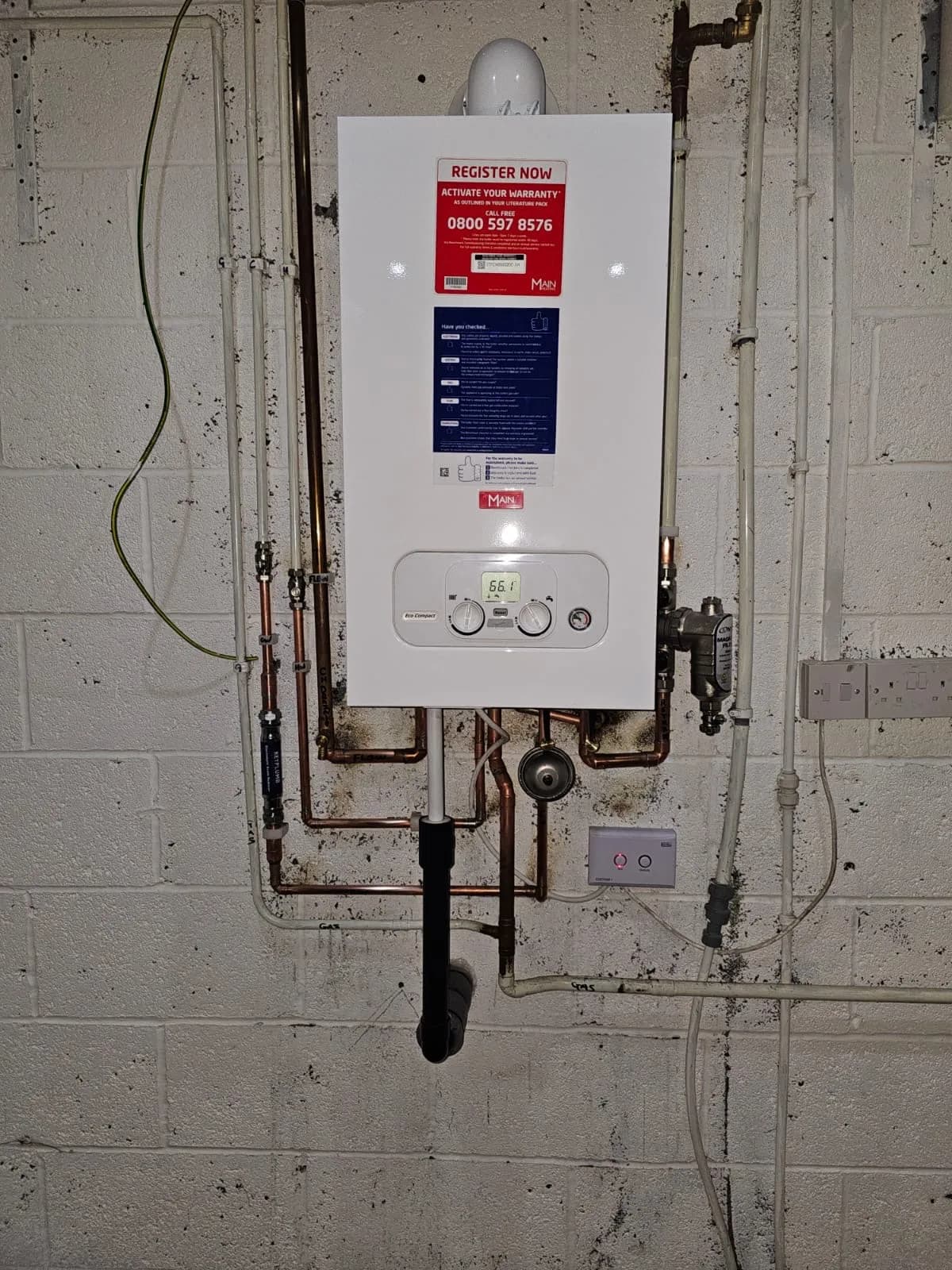Wall-mounted boiler installed on a block wall with copper pipework and isolation valves