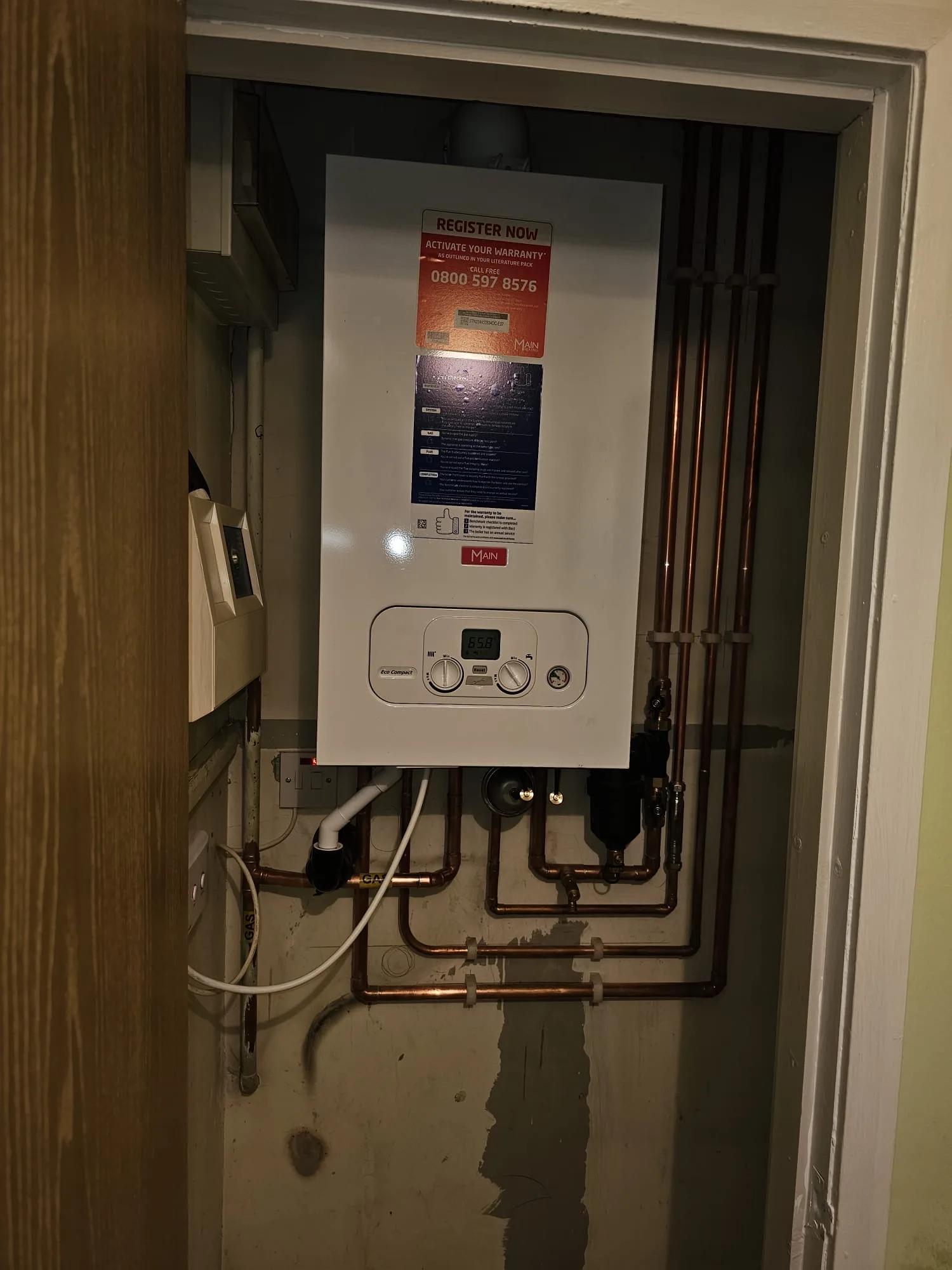 Compact combi boiler installed inside a kitchen cupboard with gas and water pipework