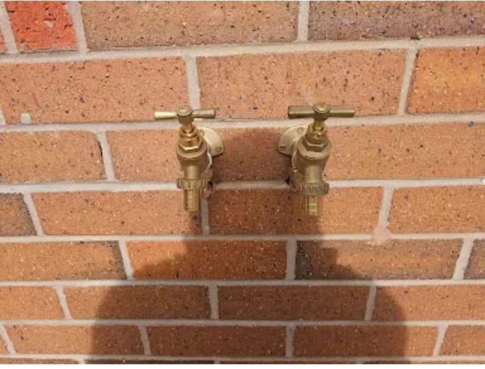 Twin outdoor brass taps installed on an exterior brick wall